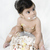 Close-up of a baby boy sitting in front of a cake with icing on his body