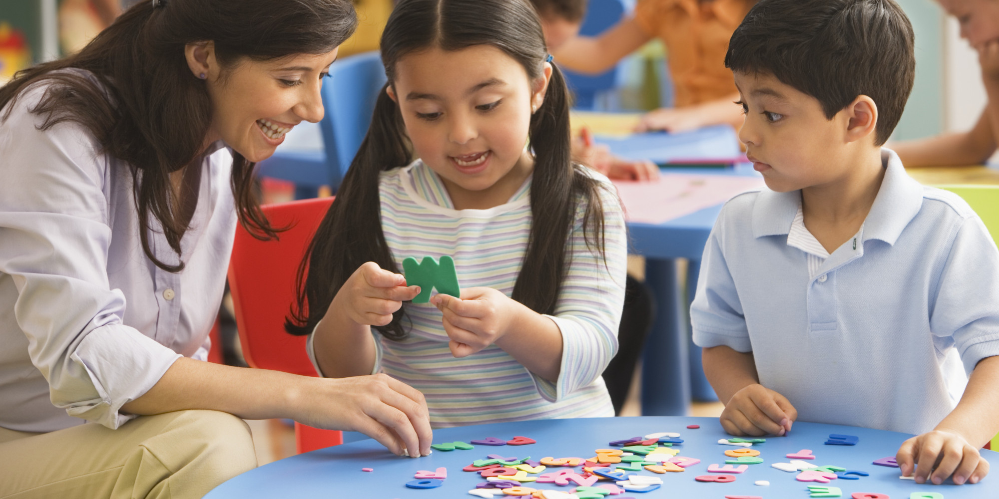  A teacher is sitting at a table with two children, they are playing an educational game with foam letters.