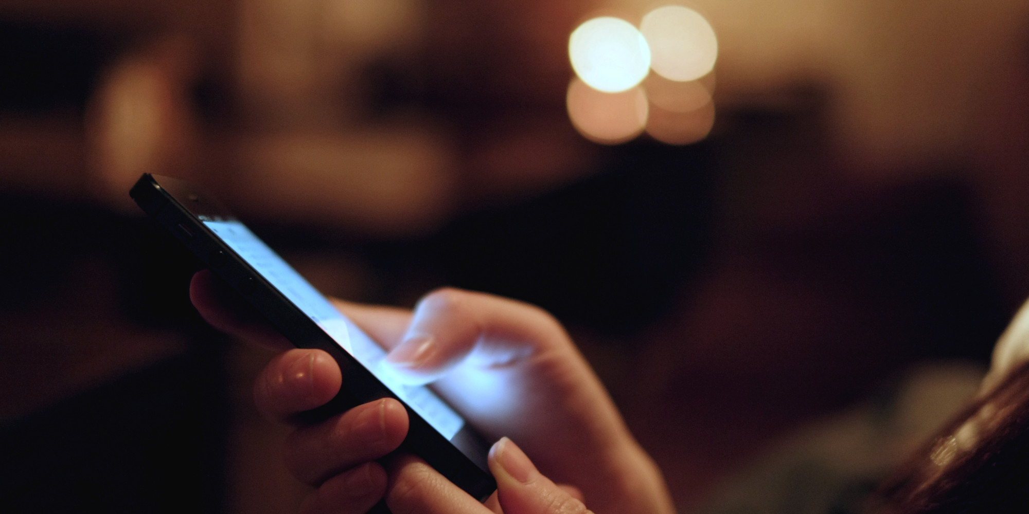 Woman's hand holding a mobile phone on the side with the white screen glowing.